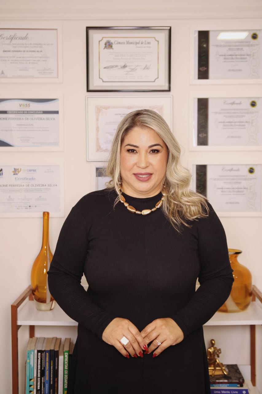 Psicóloga Simone Silva de preto, em pé com certificados ao fundo